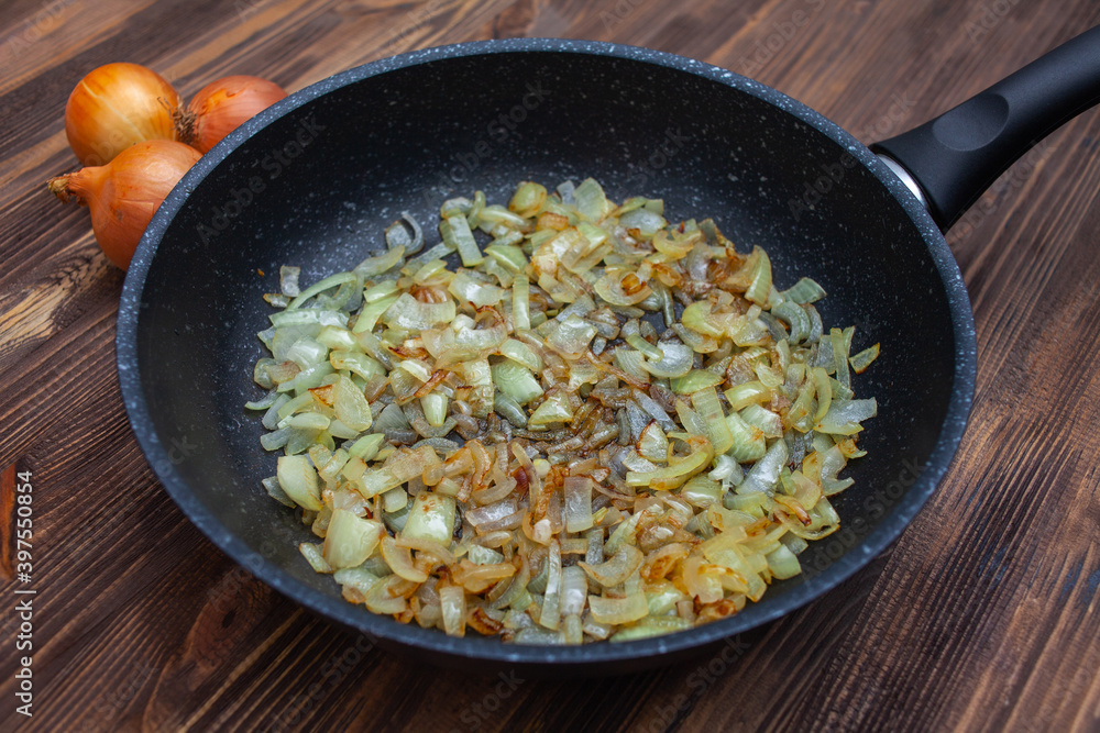 fried onions in a pan, top view. Brown wooden background, three bulbs