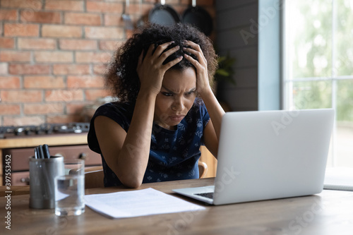 Fotografie Confused young african ethnicity woman looking at computer screen, feeling stressed of reading bad news, getting dismissal notice by email, bank loan rejection notification, unlucky people concept