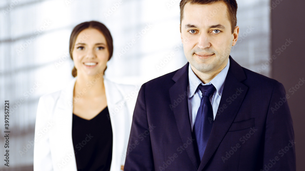 Portrait of a middle aged businessman in a dark blue suit, standing in an office with a colleague. Concept of success in a business Portrait of a middle aged businessman in a dark blue suit, standing in an office with a colleague. Concept of success in a business