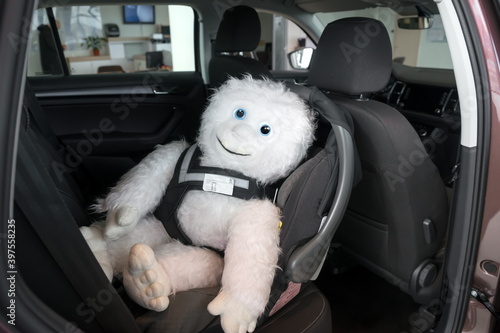 Fototapeta Naklejka Na Ścianę i Meble -  The soft toy is located in the infant car seat, fastened with a dog safety belt, inside the car.