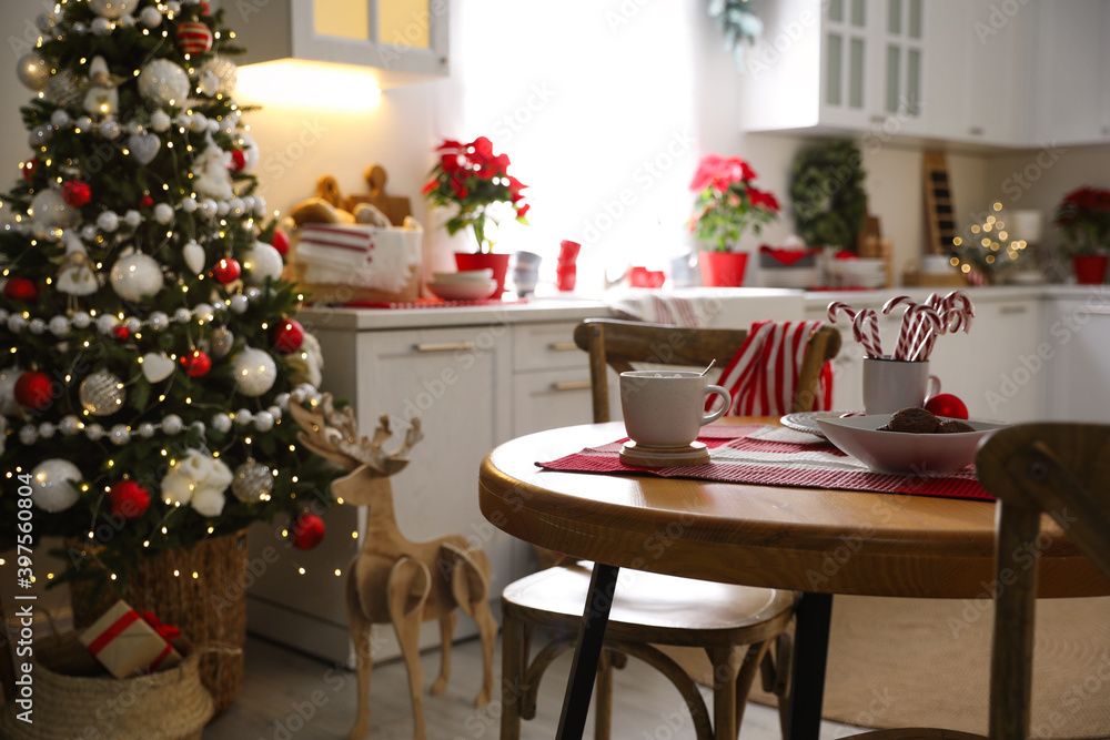 Cup of drink and candy canes on wooden table near Christmas tree in kitchen interior