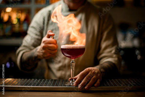 bartender carefully make fire over glass with foam cocktail on bar counter