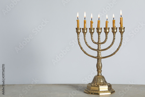 Golden menorah with burning candles on table against light grey background, space for text photo