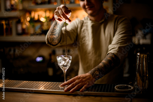 view on man bartender with long bar spoon stir the ice cubes in wine glass