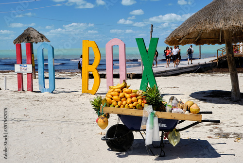 carreton con fruta en una playa paradisiaca con unas letras de colores detras