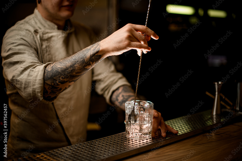 man at bar holding long bar spoon stir the ice cubes in old fashioned glass