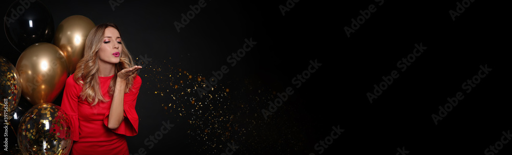Beautiful woman with balloons blowing away golden glitters on dark background, space for text. Christmas party, banner design Beautiful woman with balloons blowing away golden glitters on dark background, space for text. Christmas party, banner design