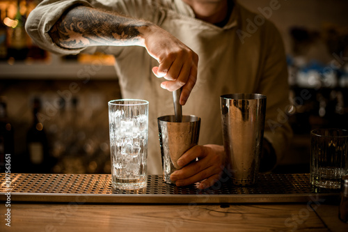 male bartender prepares cocktail in shaker cup using the muddler photo