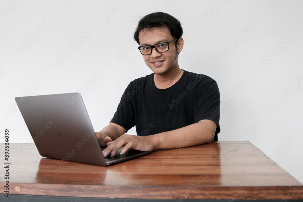 Young Asian man is serious work or thinking in the front the laptop. Indonesia Man wear black shirt Isolated grey background.