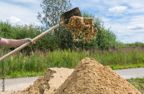 a shovel worker throws quarry sand into a large pile