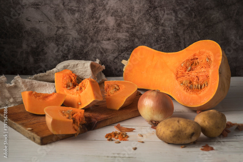 Selective focus shot of Butternut squash sliced on a cutting board with onion and potatoes