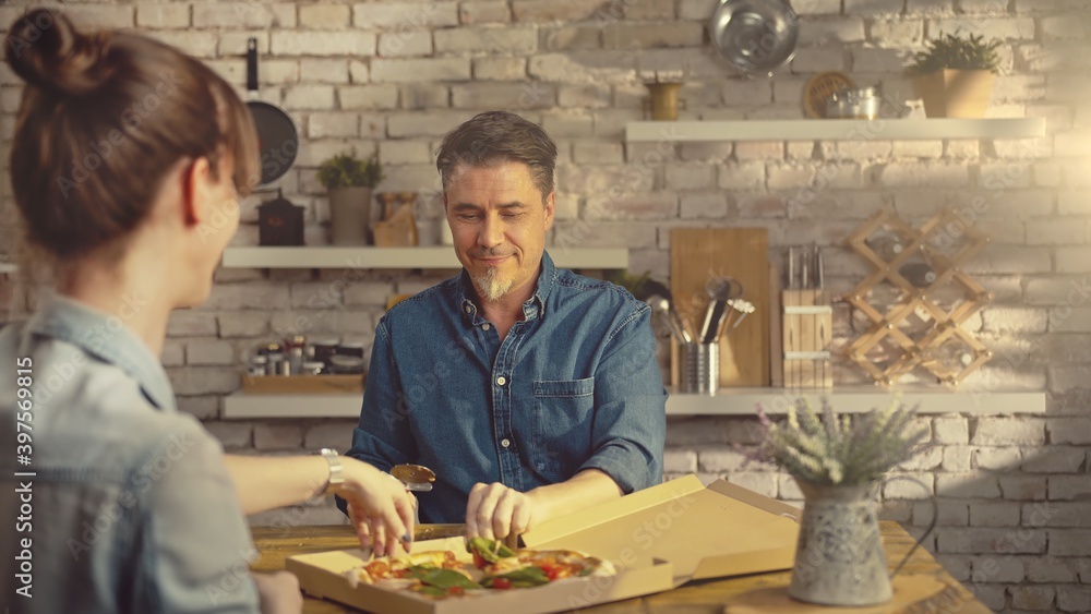 Casual couple eating take away pizza from food box. Man sharing pizza on kitchen table at home. Casual couple eating take away pizza from food box. Man sharing pizza on kitchen table at home.