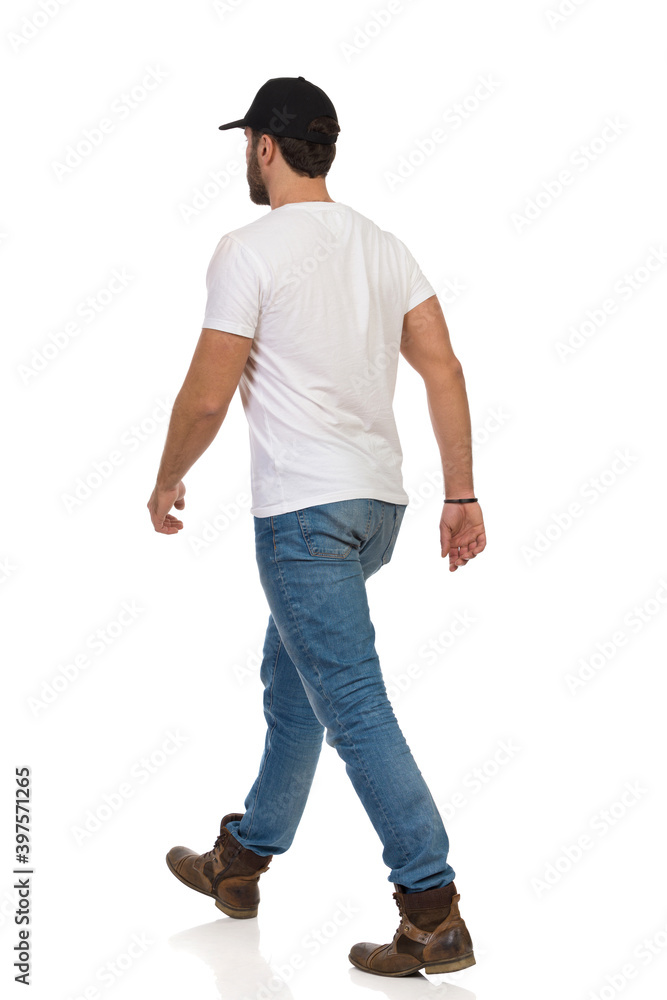 Walking Man In Boots, Jeans, White T-shirt And Black Cap. Rear Side View.  Photos | Adobe Stock