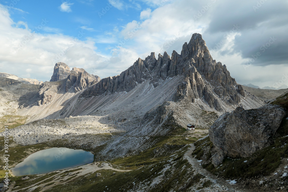 Small, navy blue lakes at the bottom of the valley in Italian Alps. The lakes are surrounded by high and steep peaks. The slopes are lush green. The sky is full of soft clouds. Raw landscape. Remedy