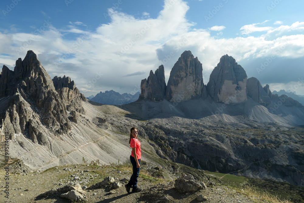 A woman in hiking outfit standing with her arms wide open and enjoying the view on the famous Tre Cime di Lavaredo (Drei Zinnen), mountains in Italian Dolomites. Desolated and raw landscape. Freedom