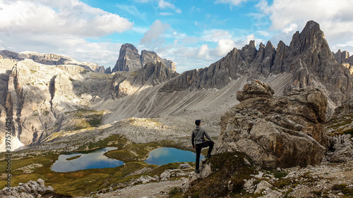 A man hiking with the view on small  navy blue lakes at the bottom of the valley in Italian Alps. The lakes are surrounded by high and steep peaks The sky is full of soft clouds. Raw landscape. Remedy