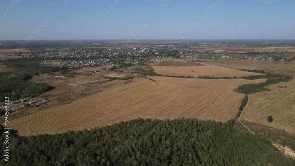 Wide yellow field. Trees grow around. The field was captured from a drone. In the distance, residential buildings can be seen in the background. Wide yellow field. Trees grow around. The field was captured from a drone. In the distance, residential buildings can be seen in the background.