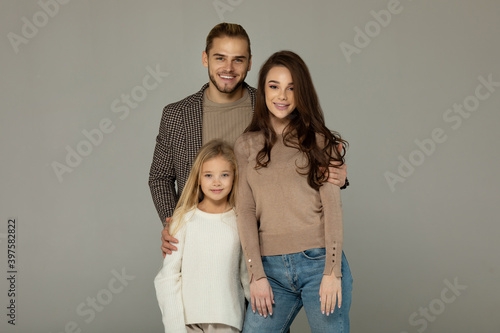 Portrait of attractive father, daughter and mother embracing together in front of grey background.