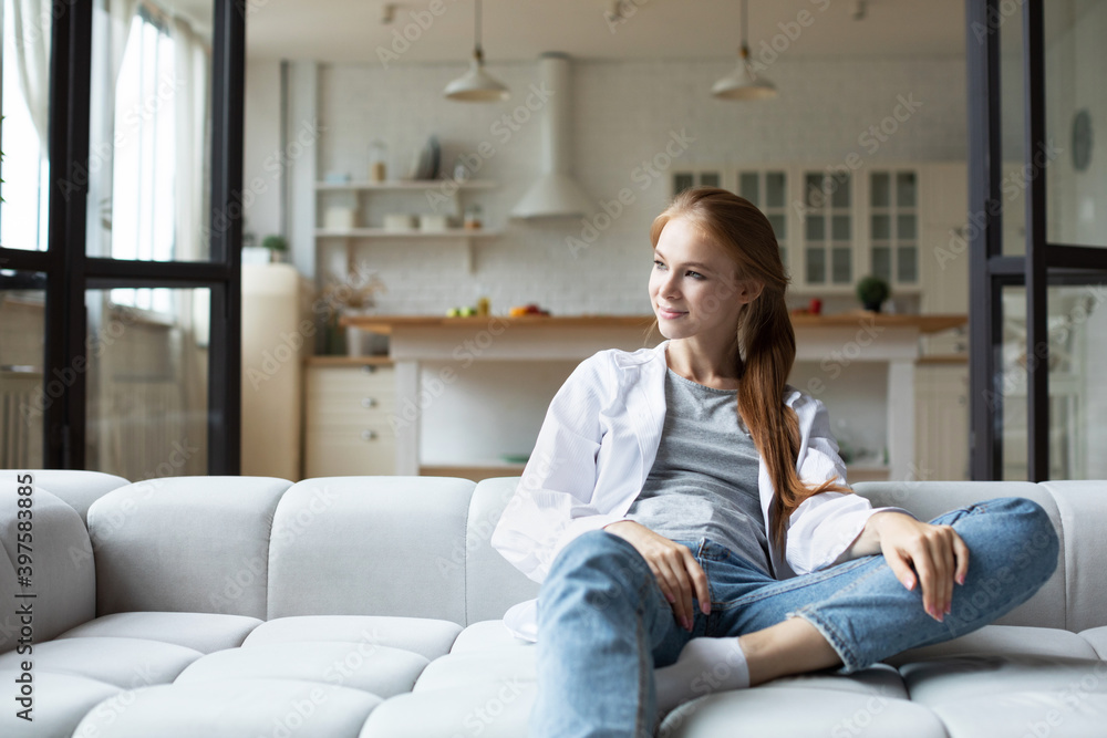 Smiling woman sitting on sofa at home, enjoying lazy weekend alone in own apartment. Smiling woman sitting on sofa at home, enjoying lazy weekend alone in own apartment.