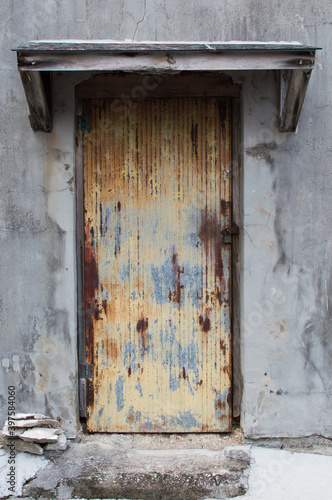 古いコンクリートの建物の赤錆びた鉄板の扉 © Ta-c
