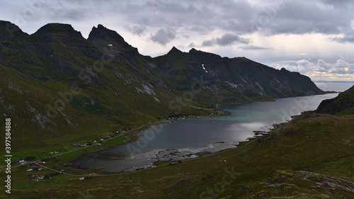 Beautiful panoramic view of fjord Skjelfjorden on Moskenesøya island, Lofoten, Norway with small village and rugged mountains covered by green grass on cloudy day in late summer.