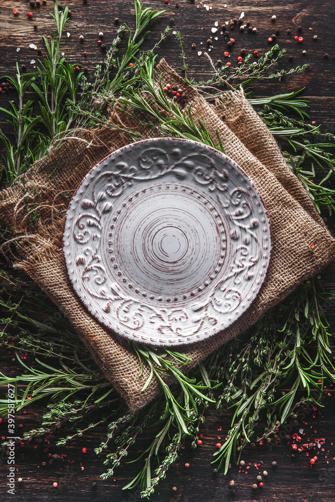 An empty plate in the middle of fragrant herbs on the table. Serving with thyme and rosemary burlap. Breakfast lunch or dinner in a rustic style An empty plate in the middle of fragrant herbs on the table. Serving with thyme and rosemary burlap. Breakfast lunch or dinner in a rustic style