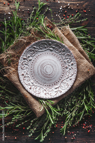 An empty plate in the middle of fragrant herbs on the table. Serving with thyme and rosemary burlap. Breakfast lunch or dinner in a rustic style