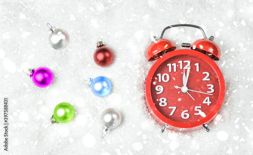 Red alarm clock with colored Christmas balls in the snow. Space for text. New Year and Christmas concept