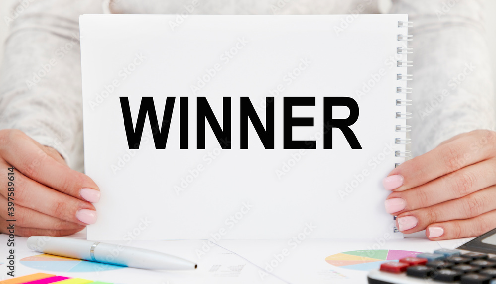 The girl holds a notebook with the text WINNER in front of her. The girl holds a notebook with the text WINNER in front of her.
