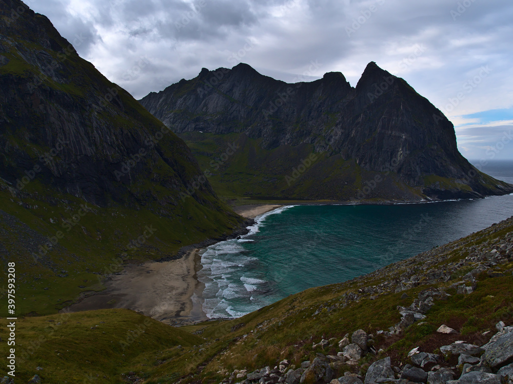 Stunning view of Kvalvika Beach with wild surf surrounded by steep rugged mountains and rocky meadows on cloudy day in late summer on Moskenesøya island, Lofoten, Norway, Scandinavia.