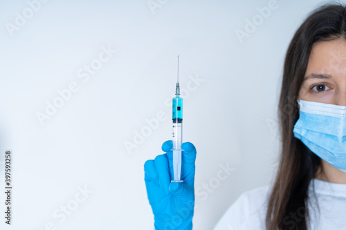 Young female doctor in a medical mask and gloves holds a syringe with a coronavirus vaccine and a vaccine chip inside. Conspiracy theory. Chipping people