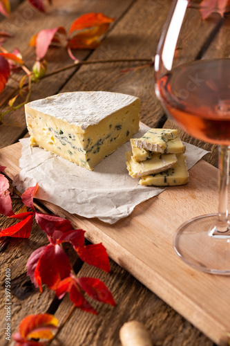Glass of rose wine on a wooden background, background of red grape leaves, blue cheese and wine