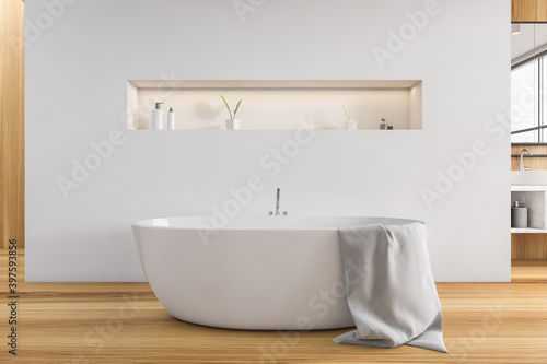 Wooden and white bathroom with white bathtub on wooden floor, deck for gels