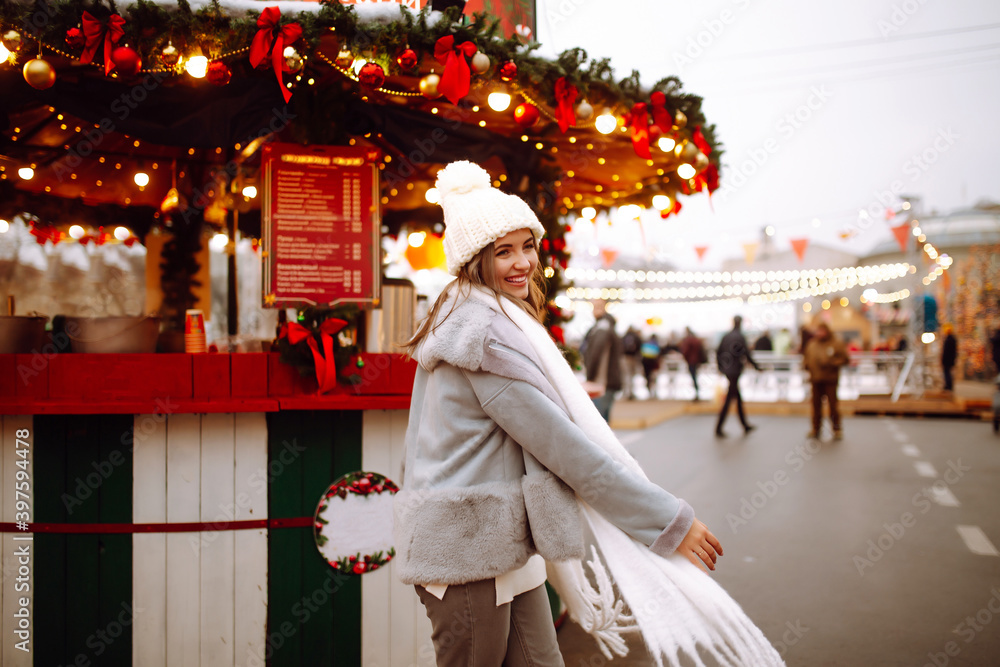 Beautiful woman enjoys winter holidays walking on Christmas market. Young woman posing on  festive street. New year.