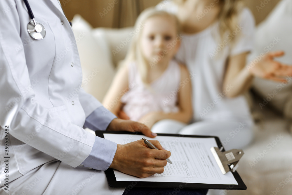 Doctor and patient. Pediatrician using clipboard while examining little girl with her mother at home. Sick and unhappy child at medical exam. Medicine concept Doctor and patient. Pediatrician using clipboard while examining little girl with her mother at home. Sick and unhappy child at medical exam. Medicine concept