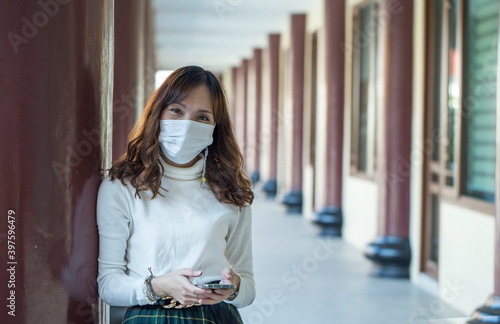 Asian beautiful woman wearing a face mask to prevent contracting the epidemic  Covid 19c stands using her smartphone to reply to e-mail messages at the airport.