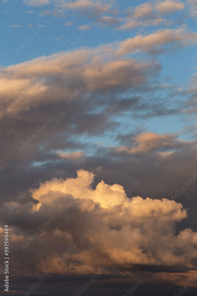 Sunset sky. Big white fluffy storm cumulus clouds in yellow orange sunlight on blue sky background texture