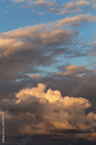 Sunset sky. Big white fluffy storm cumulus clouds in yellow orange sunlight on blue sky background texture