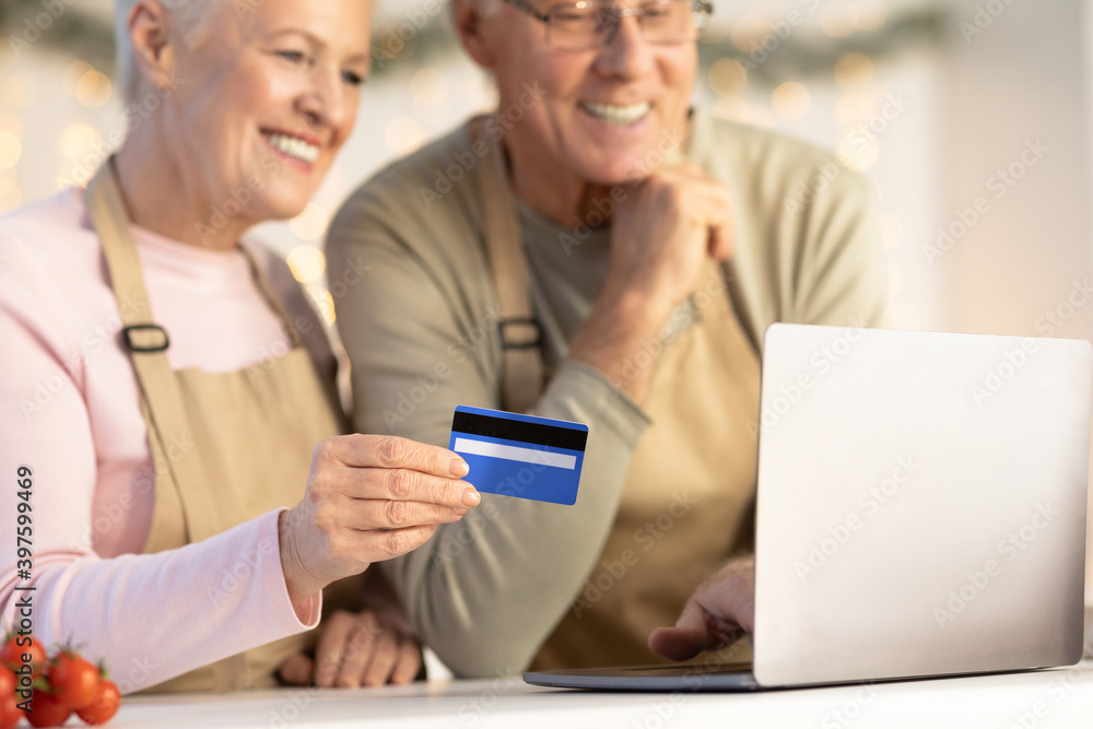 Elderly Couple Using Credit Card And Laptop Buying Groceries Indoors