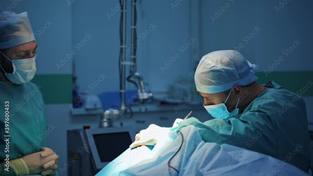 Male surgeons during operation. Doctors in medical uniform and mask doing a plastic surgery on a patient in the modern medical room. Male surgeons during operation. Doctors in medical uniform and mask doing a plastic surgery on a patient in the modern medical room.