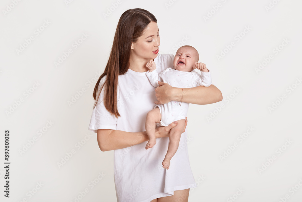 Young beautiful mother with cute little crying baby posing isolated over white background, mommy calm down her daughter, lady wearing casual t shirt, newborn in bodysuit. Young beautiful mother with cute little crying baby posing isolated over white background, mommy calm down her daughter, lady wearing casual t shirt, newborn in bodysuit.