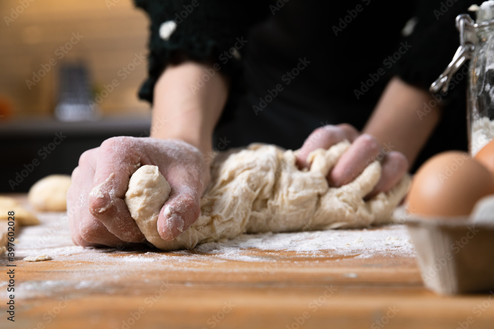 Young beautiful woman kneading dough at a wooden table in kitchen. Housewife hobbies concept.