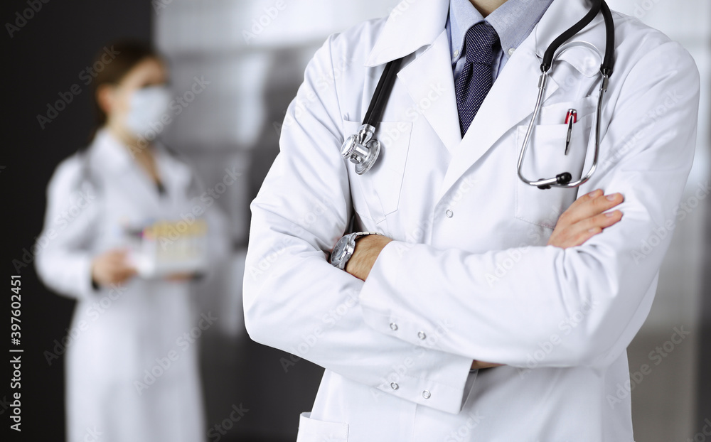 Unknown male doctor in protective mask standing with arms crossed in clinic. Medicine concept during Coronavirus pandemic. Covid 2019 Unknown male doctor in protective mask standing with arms crossed in clinic. Medicine concept during Coronavirus pandemic. Covid 2019