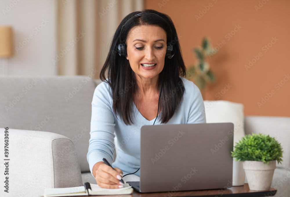 Mature woman in headset writing and using laptop at home Mature woman in headset writing and using laptop at home