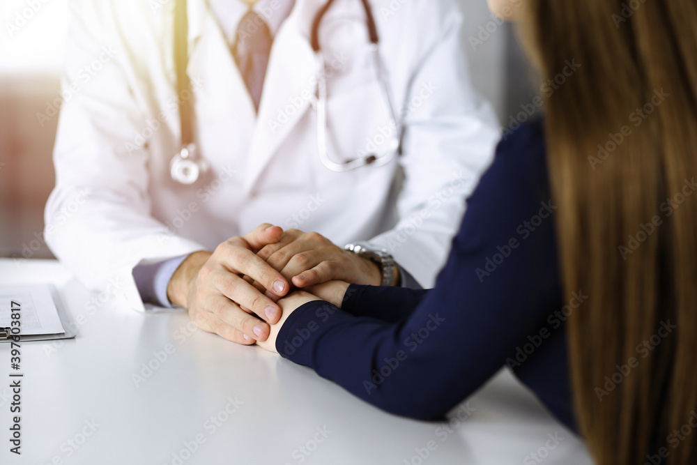 Fototapeta premium Unknown man-doctor reassuring his female patient, close-up. Perfect medical service, empathy in medicine during Coronavirus pandemic