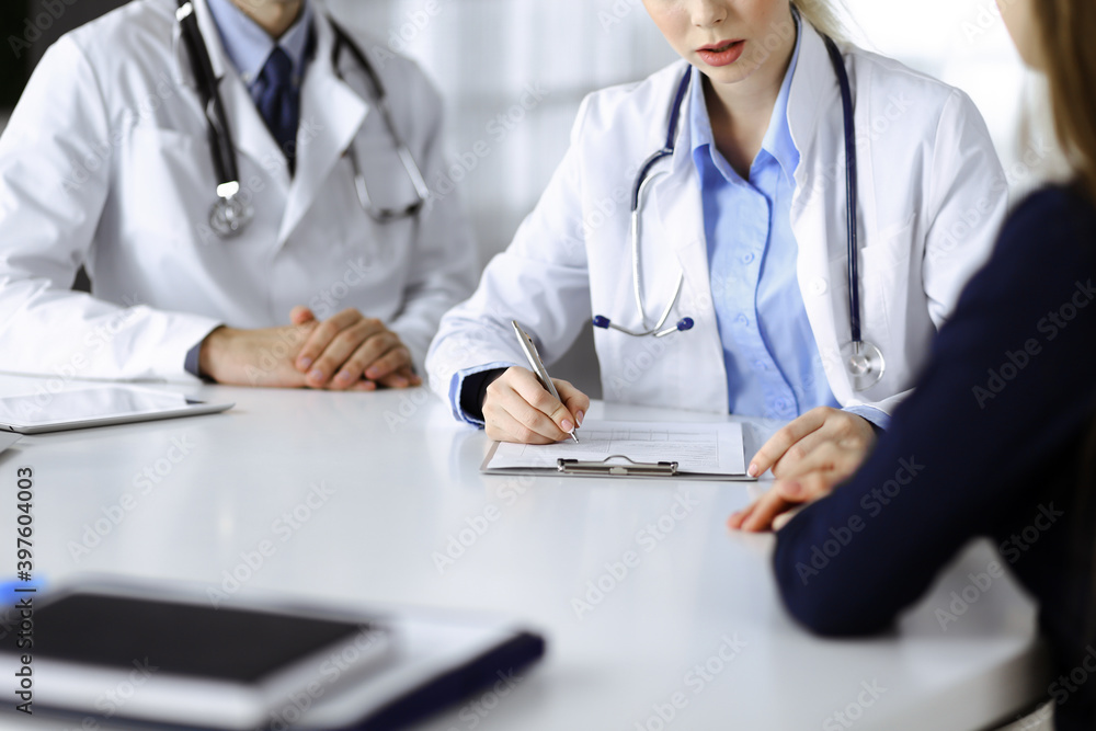 Unknown woman-doctor with male colleague are consulting patient woman while sitting at the desk in modern clinic, close-up. Perfect medical service, medicine during Coronavirus pandemic. Covid 2019 Unknown woman-doctor with male colleague are consulting patient woman while sitting at the desk in modern clinic, close-up. Perfect medical service, medicine during Coronavirus pandemic. Covid 2019