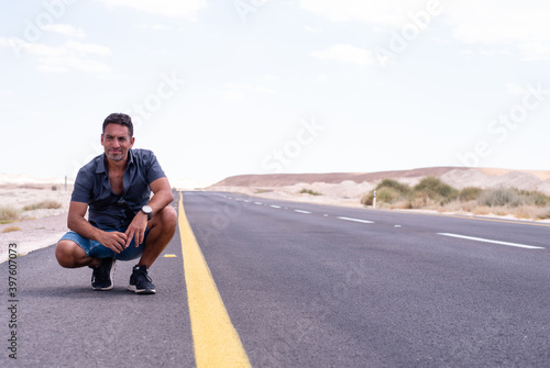 one man sits on the road highway in gray t-shirt. time of travel, space for text. road in desert. no have cars. yellow line on the road. road empty