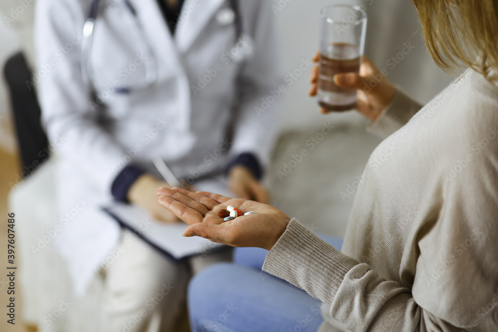 Close-up woman-patient holding pills near her doctor, time to take medications, cure for headache or remedy pain killer drugs. Stay at home concept during Coronavirus pandemic and self isolation Close-up woman-patient holding pills near her doctor, time to take medications, cure for headache or remedy pain killer drugs. Stay at home concept during Coronavirus pandemic and self isolation