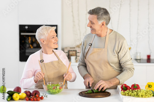 Cheerful Aged Couple Cooking Salad Preparing Dinner In Modern Kitchen