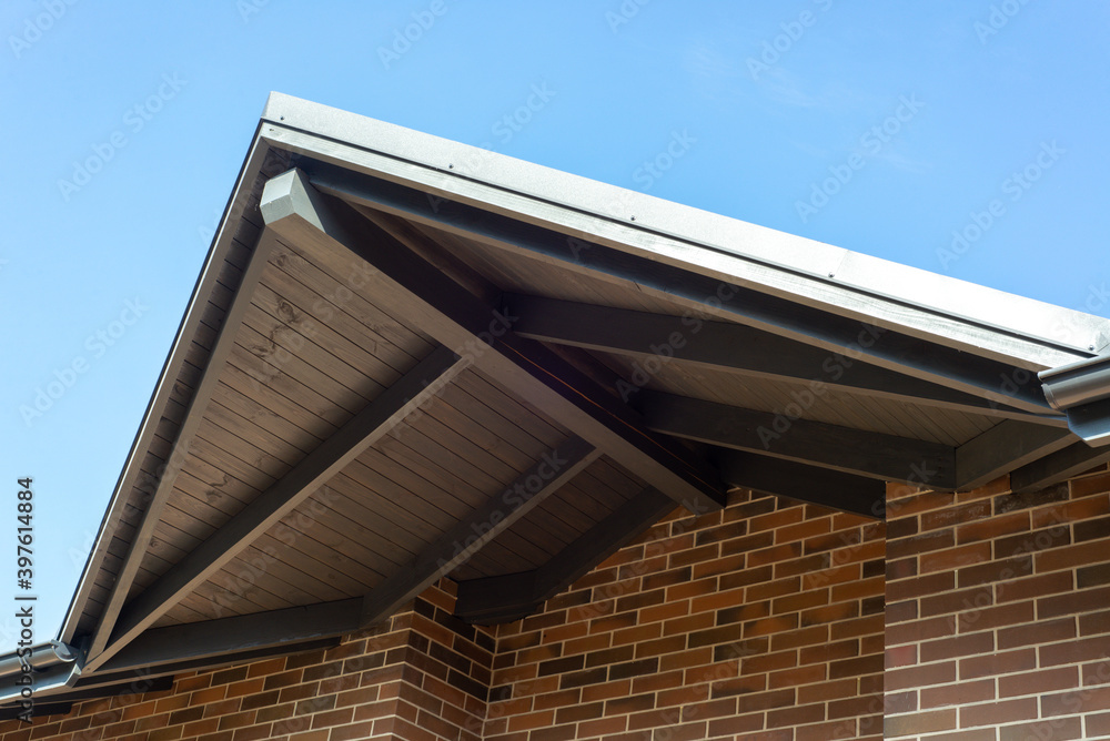 Obraz premium Part of wall made of the brown brick, windows and fragment of roof of modern private dwelling house against of sky